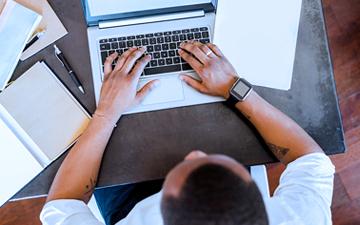 Aerial view of a man wearing a black smartwatch typing on a laptop